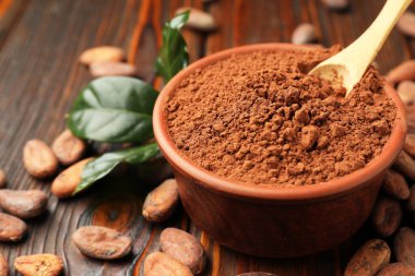 Doğal kakao çekirdekleri, toz ve yeşil yapraklar ahşap masada, yakın plan.