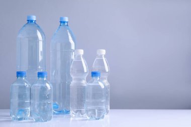 Beyaz masada gri arkaplan ile farklı boyutlarda su şişeleri, metin için boşluk