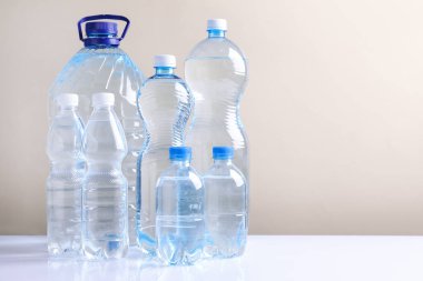 Beyaz masada bej arka planda farklı boyutlarda su şişeleri var. Metin için boşluk