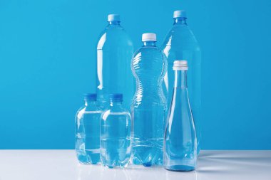 Açık mavi arka planda beyaz masada farklı boyutlarda su şişeleri