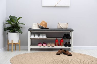 Farklı ayakkabı, aksesuarlar ve açık gri duvarın yanındaki ev bitkilerinden oluşan ayakkabı deposu.