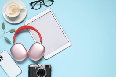 Kulaklıklar, akıllı telefon, tablet, klasik kamera, açık mavi arka planda kahve ve bardaklar, düz konum. Metin için boşluk