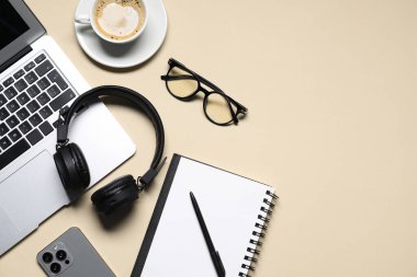 Kulaklıklar, dizüstü bilgisayarlar, akıllı telefonlar, gözlükler, bej arka planda kahve ve kırtasiye malzemeleri, düz yatak. Metin için boşluk