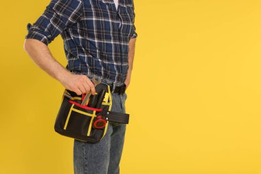 Sarı arka planda alet kemeri olan profesyonel müteahhit, yakın plan. Metin için boşluk