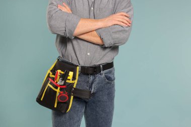 Açık mavi arka planda alet kemeri olan profesyonel inşaatçı, yakın plan