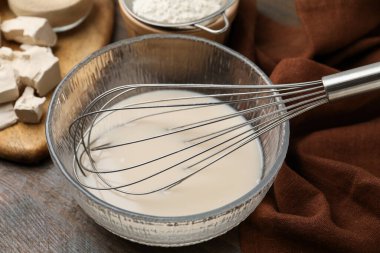 Cam kasede sıvı hamur, çırpma, maya ve un ahşap masada, yakın plan.