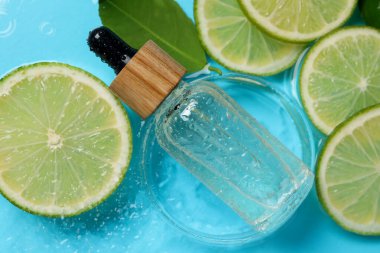 Bir şişe cilt bakımı ürünü, limon dilimleri ve açık mavi arkaplanda yeşil yaprak, düz bir zemin.