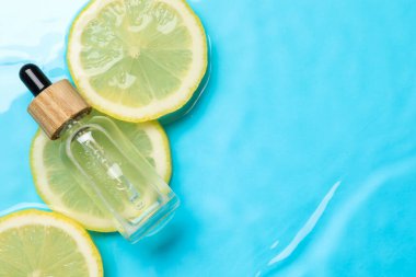 Bir şişe cilt bakımı ürünü ve açık mavi arka planda limon dilimleri. Metin için boşluk
