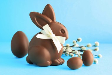 Çikolatalı Paskalya tavşanı, yumurtalar ve söğüt dalları açık mavi arka planda, yakın plan