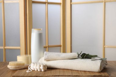 Temiz waffle havluları, okaliptüs dalları ve kapalı masa üzerindeki kozmetik ürünler.