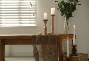 Zarif şamdanlar, yanan mumlar ve kapalı masa üzerinde dalları olan vazolar.