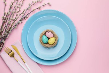 Paskalya kutlaması. Boyalı yumurtalar, söğüt dalları ve pembe arka planda çatal bıçak takımları ile şenlik masası, metin için yeri olan düz bir yer.