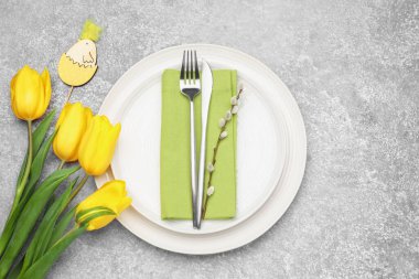 Paskalya kutlaması. Lale çiçekleri, çatal bıçak takımları ve söğüt dallarıyla bezenmiş gri dokulu masa, düzlük ve metin için yer