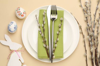 Paskalya kutlaması. Renkli yumurtalar, söğüt dalları ve bej arka planda çatal bıçak takımı olan şenlik masası.