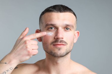 Yüzüne açık gri arka planda krem süren yakışıklı bir adam.