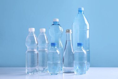 Açık mavi arka planda beyaz masada farklı boyutlarda su şişeleri