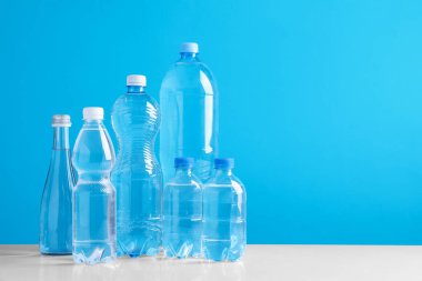 Beyaz masada farklı boyutlarda su şişeleri açık mavi arkaplan, metin için boşluk
