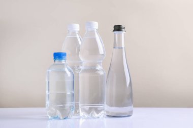 Beyaz masada bej arka planda farklı boyutlarda su şişeleri
