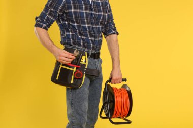 Sarı arka planda alet kemeri ve kablo makarası olan profesyonel müteahhit, yakın plan.