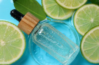 Bir şişe cilt bakımı ürünü, limon dilimleri ve açık mavi arkaplanda yeşil yaprak, düz bir zemin.