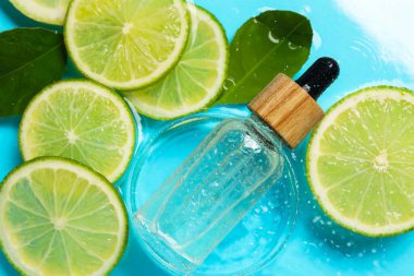 Bir şişe cilt bakımı ürünü, limon dilimleri ve açık mavi arka planda yeşil yapraklar, düz bir zemin.