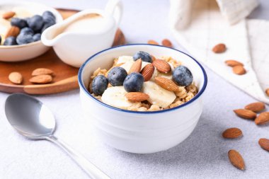 Bademli yulaf gevreği, yaban mersini, muz ve süt açık gri masada, yakın plan.