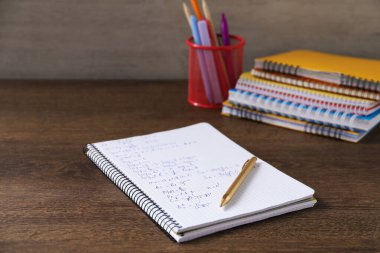 Ev ödevi. Matematik formülleri ve ahşap masa üzerindeki farklı kırtasiyeli defter.