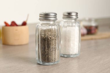 Beyaz duvarın yanındaki ahşap masada baharatlı tuzluk ve biberlikler.