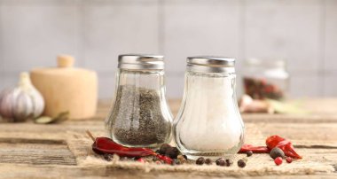 Ahşap masaya baharatlı tuzluk ve biberlikler seramik duvara karşı, yakın plan.