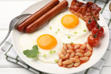 Geleneksel İngiliz kahvaltısı. Lezzetli, güneşli, pastırmalı yumurta ve sosisler beyaz ahşap masada servis ediliyor, yakın plan.