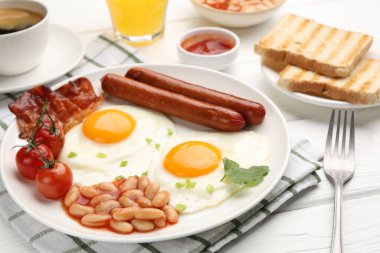 Geleneksel İngiliz kahvaltısı. Lezzetli, güneşli, pastırmalı yumurta ve sosisler beyaz ahşap masada servis ediliyor, yakın plan.