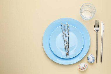 Paskalya kutlaması. Renkli yumurtalar, söğüt dalları ve bej arka planda çatal bıçak takımları olan şenlikli masa ayarı, metin için yeri olan düz bir yer.