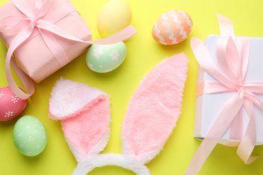 Boyalı Paskalya yumurtaları, tavşan kulaklıkları ve açık yeşil arka planda hediyeler.