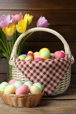 Hasır sepete boyanmış Paskalya yumurtaları ve ahşap masada güzel laleler.