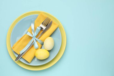 Paskalya kutlaması. Çatal bıçak takımı ve açık mavi arka planda boyalı yumurtalar, üst manzara. Metin için boşluk