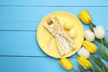 Paskalya kutlaması. Çatal bıçak takımları, laleler ve açık mavi ahşap masa üzerine boyanmış yumurtalar. Metin için boşluk
