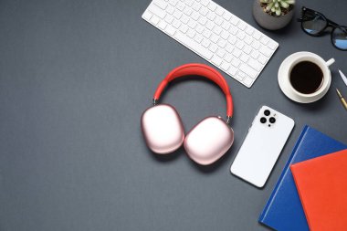 Kulaklıklar, akıllı telefon, kahve, kırtasiye malzemeleri, bardaklar, bilgisayar klavyesi ve siyah arka planda çiçek dekoru, düz yatak. Metin için boşluk