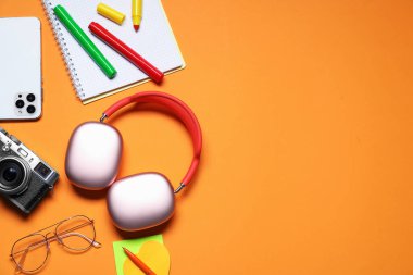 Kulaklık, akıllı telefon, klasik kamera, turuncu arka planda gözlük ve kırtasiye malzemesi, düz yatak. Metin için boşluk