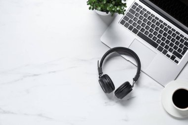 Kulaklıklar, dizüstü bilgisayarlar, kahve ve çiçek dekoru beyaz mermer masa, düz yatak. Metin için boşluk