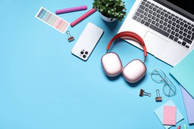 Kulaklıklar, dizüstü bilgisayarlar, akıllı telefonlar, gözlükler, kırtasiye malzemeleri ve açık mavi arka planda çiçek dekoru, düz yatak. Metin için boşluk