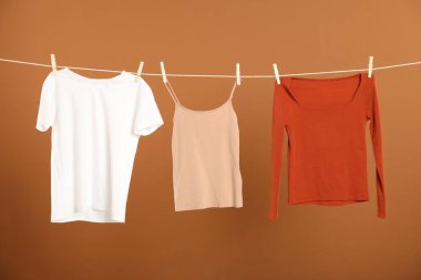 Çamaşır ipini kahverengi arka planda tutarken farklı giysiler kuruyor.