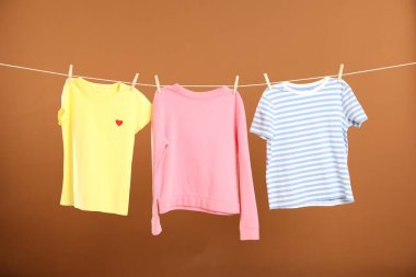 Çamaşır ipini kahverengi arka planda tutarken farklı giysiler kuruyor.