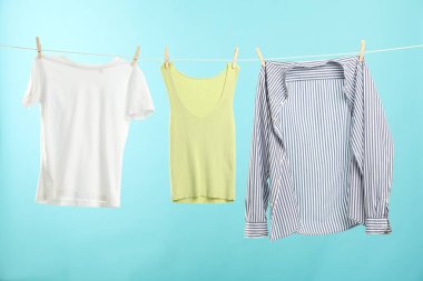 Açık mavi arka planda çamaşır ipine tutunurken farklı giysiler kuruyor