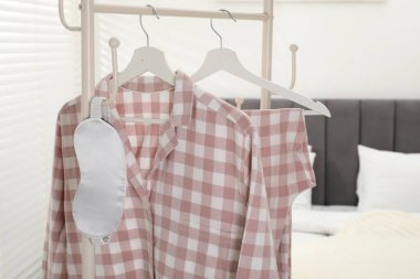 Şık pijamalar ve uyku maskesi yatağın yanındaki rafta asılı, yakın plan.