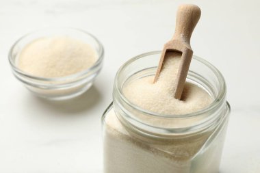 Kavanozda jelatin tozu, kepçe ve kase beyaz masada, yakın plan.