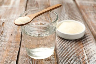 Jelatin tozu ve bir bardak su ahşap masada.