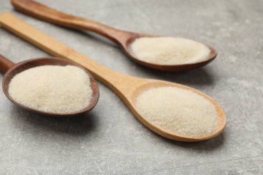 Açık gri masada kaşıklarda jelatin tozu, yakın plan.