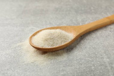 Açık gri masada kaşıkta jelatin tozu, yakın plan.