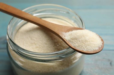 Kavanozda jelatin tozu ve açık mavi ahşap masada kaşık, yakın plan.