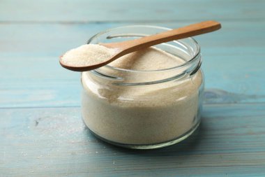 Kavanozda jelatin tozu ve açık mavi ahşap masada kaşık, yakın plan.